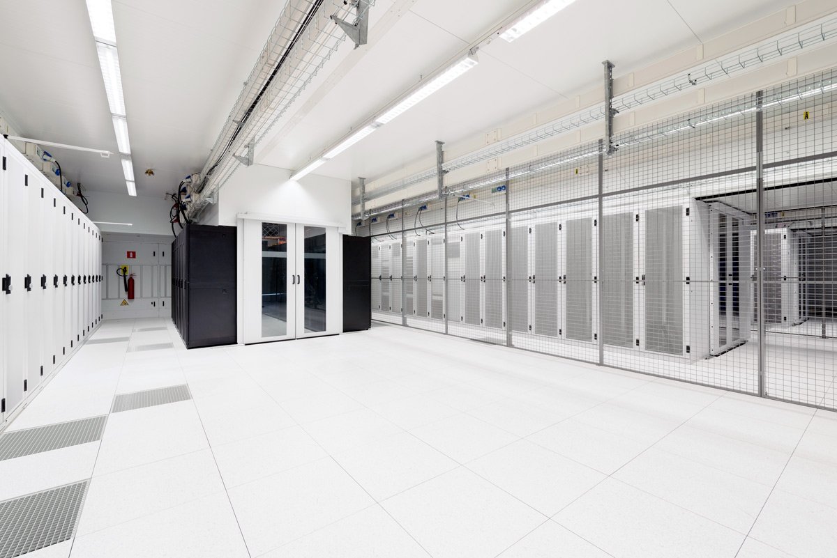 White data centre room with rows of server cabinets behind a mesh security cage and a glazed cold-aisle door