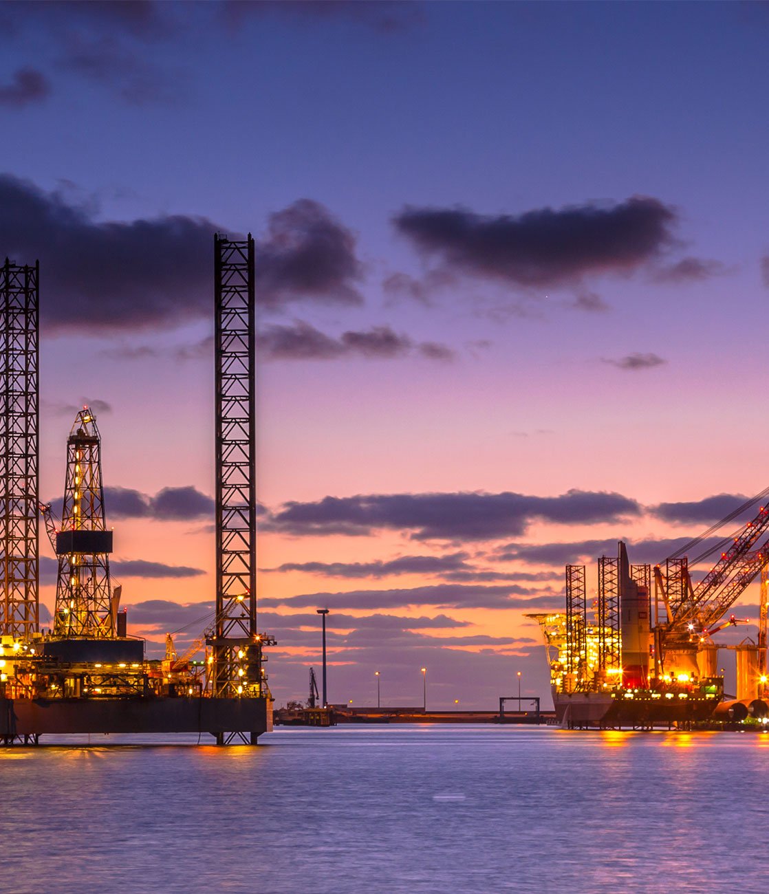 Offshore drilling rigs and a lit supply vessel at dusk, an operational environment where OT security applies